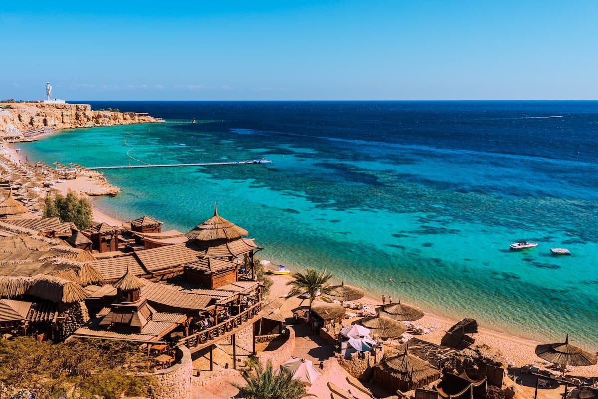 Flygfoto av en bukt vid Sharm el-Sheikh vid Röda havet — restauranger på pålar, turkost vatten med korallrev, bryggor.