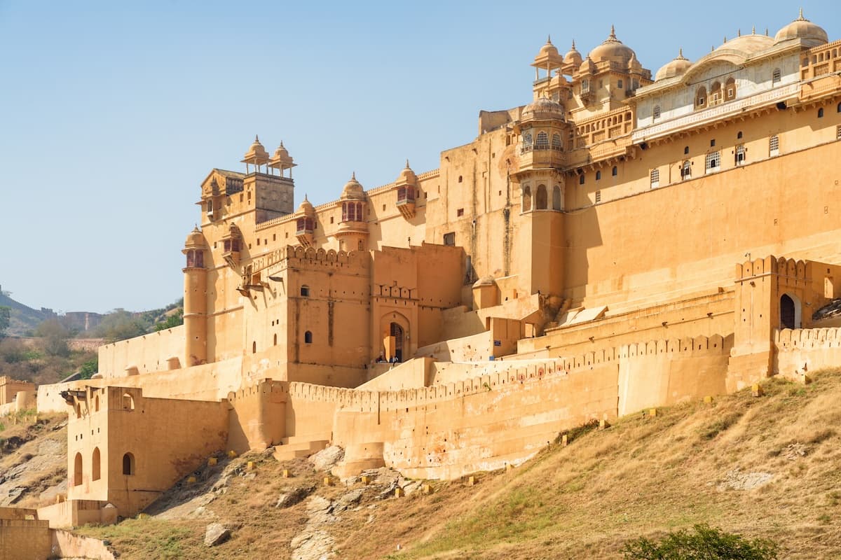 Amer Fort över Maota-sjön nära Jaipur i Rajasthan — sandstensmurar, terrasserade gårdar och Aravalli-utlöpare.